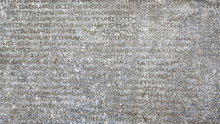Ancient Greek Writing Background, Antique Stone Inscription. Old Script Text Close-up. Gray Wall With Historic Letters. Vintage Texture With Words From Past Civilization.