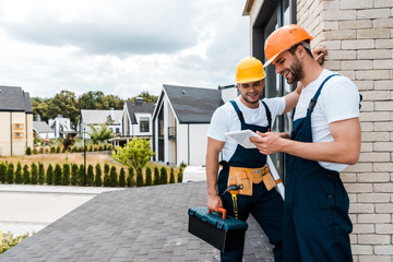 Wall Mural - happy handyman holding toolbox near cheerful coworker using digital tablet