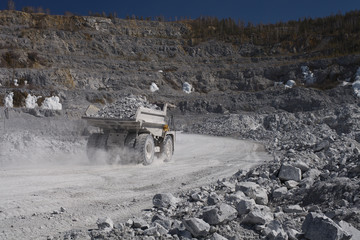 Wall Mural - Heavy dump-body truck loaded with limestone ore moves along the road in a quarry, back view. Mining industry. Heavy equipment.