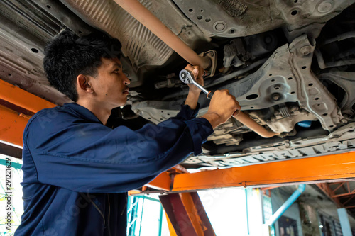Fotomural A man mechanic is fixing the engine on the car lift
