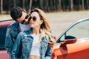 Wall Mural - attractive woman and handsome man in jackets kissing near car