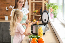 Woman And Her Little Daughter Using Modern Multi Cooker In Kitchen