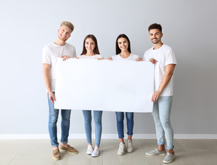 Wall Mural - Group of young people in stylish casual clothes and with blank poster near light wall