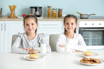 Poster - Portrait of cute twin girls drinking milk with sweets in kitchen