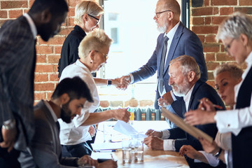 Wall Mural - Group of businessmen at table in office. Camera focused on two of them shaking hands