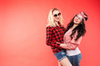 © Вячеслав Косько - Studio shot of pretty smiling blonde and brunette girlfriends in sunglasses and trendy outlooks hugging against bright red background. Isolated.