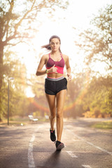 Wall Mural - Young female in sportswear running in a park