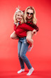 © Вячеслав Косько - Stock studio portrait of two cheerful and positive trendy girlfriends or sisters having fun. Girl in sunglasses making bunny ears to her friend with her hand while sitting on her back. Isolate on red.