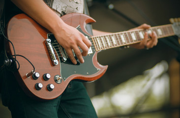 Wall Mural - The musician, dressed in a t-shirt and jeans, plays a powerful melody at the concert on a stylish red electric guitar