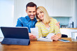© baranq - Happy couple managing home finances looking at receipts and tablet