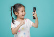 © DN6 - Excited Asian little girl is using a smartphone, empty space in studio shot isolated on colorful blue background