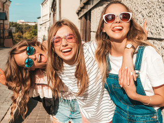 Wall Mural - Portrait of three young beautiful smiling hipster girls in trendy summer clothes. Sexy carefree women posing near wall in the street.Positive models having fun in sunglasses
