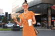 © ty - Portrait fashion woman in yellow dress walking on street and holding smartphone in her hand