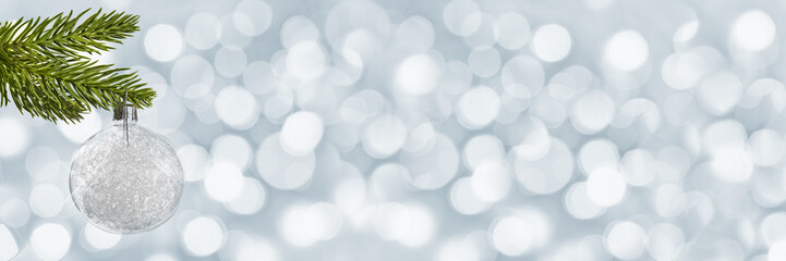 Wall Mural - Silver christmas ball hanging from a christmas tree branch on panoramic holiday lights background with copy space