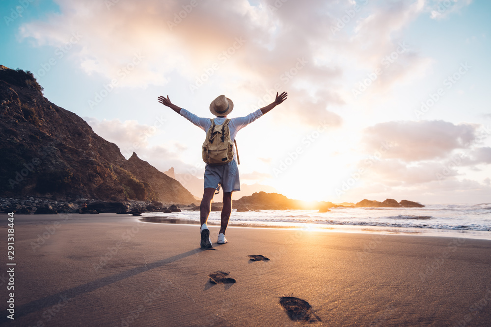 Young man arms outstretched by the sea at sunrise enjoying freedom and life, people travel wellbeing concept - obrazy, fototapety, plakaty 