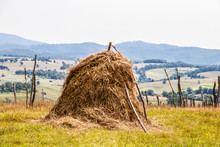 Old Fashioned Hay Stack Surrounded By Stick Fence With Farm And Hill Countryside In The Background - Georgia Eastern Europe