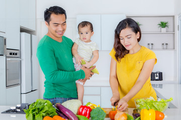 Wall Mural - Mother prepares salad with her husband and baby