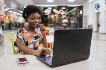 Wall Mural - Beautiful Young Dark Skinned Freelancer Woman Using Laptop Computer Sitting At Cafe Table.  Freelance Work Concept.