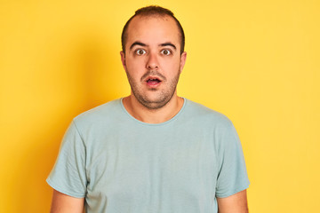 Sticker - Young man wearing green casual t-shirt standing over isolated yellow background afraid and shocked with surprise expression, fear and excited face.