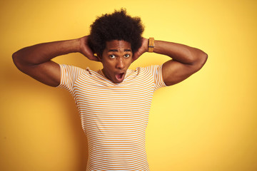 Sticker - American man with afro hair wearing striped t-shirt standing over isolated yellow background Crazy and scared with hands on head, afraid and surprised of shock with open mouth