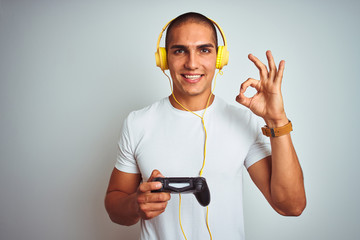 Poster - Young handsome man playing videogames using headphones over white isolated background doing ok sign with fingers, excellent symbol