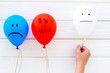 © 9dreamstudio - Negative emotions concept. Balloons with drawn faces on white wooden background top view