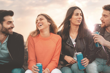 Group of young people discussing together outdoors drinking canned beers in the sunset.