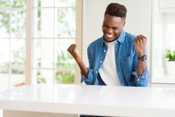 Wall Mural - Handsome african american man at home very happy and excited doing winner gesture with arms raised, smiling and screaming for success. Celebration concept.