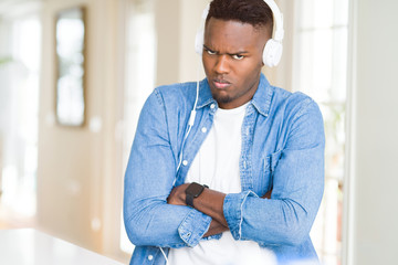 Poster - African american man wearing headphones listening to music skeptic and nervous, disapproving expression on face with crossed arms. Negative person.