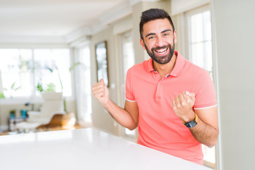 Canvas Print - Handsome hispanic man wearing casual t-shirt at home celebrating surprised and amazed for success with arms raised and open eyes. Winner concept.