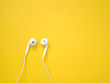 White earphones on yellow background. Earphones for listening to music and sound on portable devices.