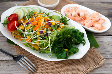 Fresh salad plate with shrimp, salmon, tomato and mixed greens  on wooden background .