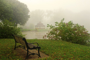 Wall Mural - early autumn foggy morning landscape.scenic view with trees, wooden gazebo and bench on a green gras