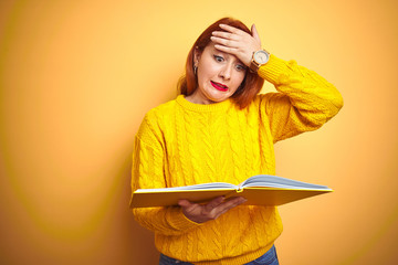 Poster - Young redhead student woman reading book standing over yellow isolated background stressed with hand on head, shocked with shame and surprise face, angry and frustrated. Fear and upset for mistake.