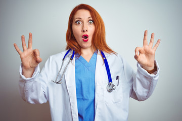 Poster - Young redhead doctor woman using stethoscope over white isolated background looking surprised and shocked doing ok approval symbol with fingers. Crazy expression