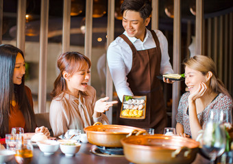 Wall Mural - waiter  bring  egg dumpling for hot pot  and serving group of friends in restaurant