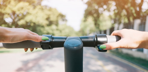 Woman riding an e-scooter in summer park, point of view.