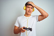 © Krakenimages.com - Young asian chinese gamer man playing video game standing over isolated white background stressed with hand on head, shocked with shame and surprise face, angry and frustrated. Fear and upset