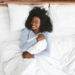© Prostock-studio - Top view of smiling woman waking up in her bed