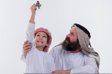 Arabic grandather and grandson playing together indoors using toy aircraft.