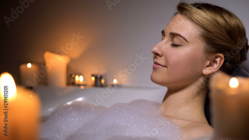 Fotografía Young female relaxing in warm bath with foam bubbles and candles, evening