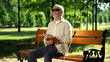 © motortion - Blind pensioner reading braille book, sitting on bench in summer park, resting