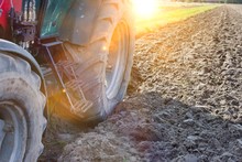 Low Angle View Of Tractor Wheel In Field With Yellow Lens Flare In Background