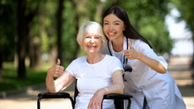 Nurse And Old Handicapped Woman Smiling At Camera And Showing Thumbs-up Gesture