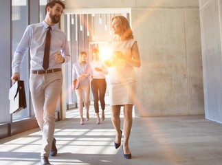 Business poeple walking while takling in office hall with yellow lens flare in background