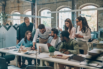 Wall Mural - Group of young modern people in smart casual wear communicating and using modern technologies while working in the office