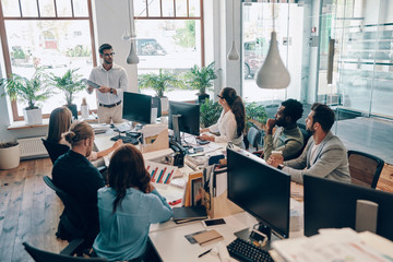 Wall Mural - Group of young modern people in smart casual wear communicating and using modern technologies while working in the office