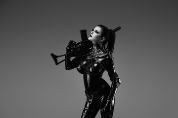 Portrait of a young woman in latex jumpsuit holding a machine gun in her hands	