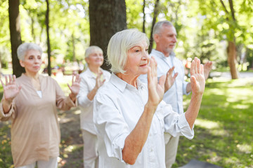 Senior woman practicing qigong with friends outdoors