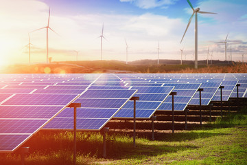 Solar panel with wind turbines against mountains and blue sky as background - image